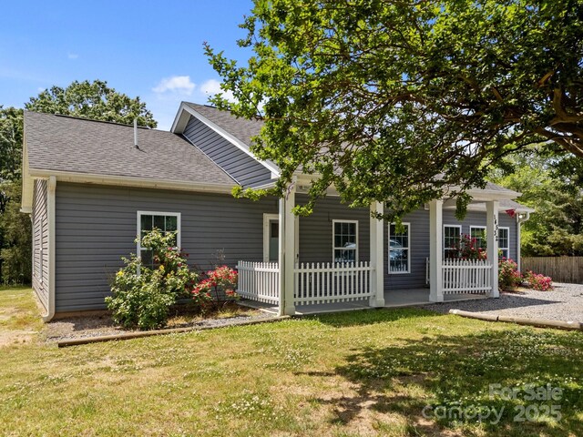 rear view of house with a lawn, fence, a shingled roof, and a porch