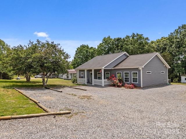 rear view of house featuring a shingled roof, a yard, covered porch, and gravel driveway