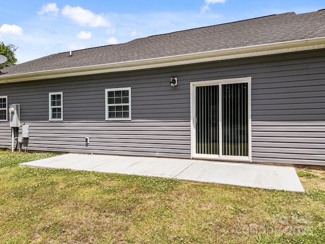 rear view of property featuring a lawn, a patio, and roof with shingles