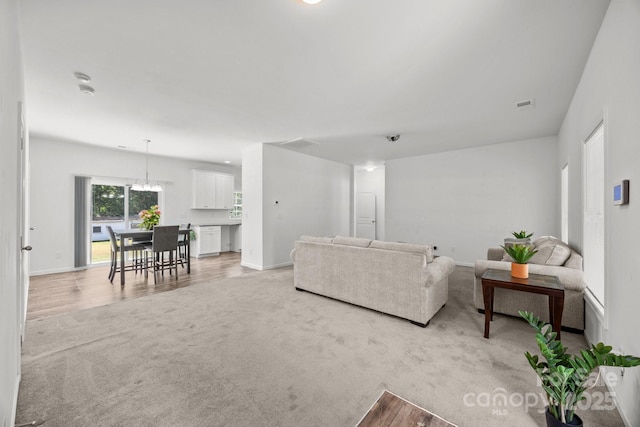 living area with light colored carpet, baseboards, a chandelier, and visible vents