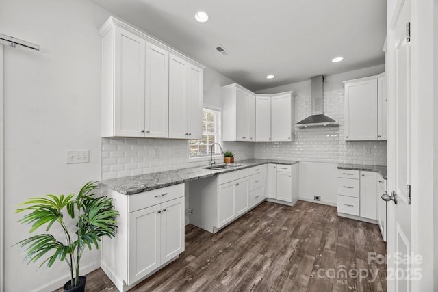 kitchen with dark wood-style flooring, light stone counters, a sink, and wall chimney exhaust hood