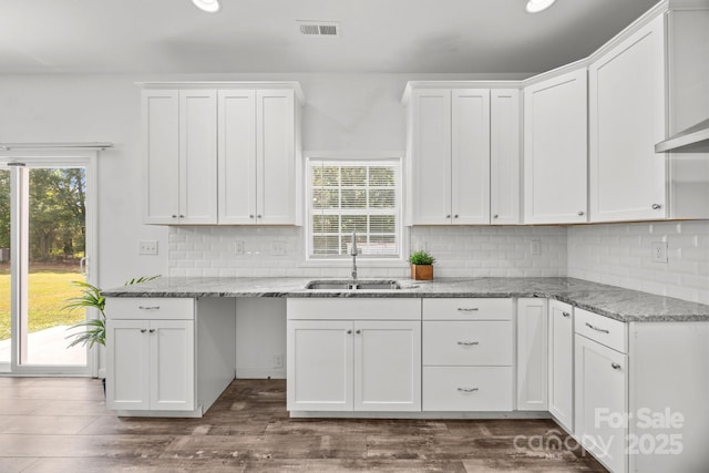 kitchen with visible vents, white cabinets, light stone counters, a sink, and backsplash