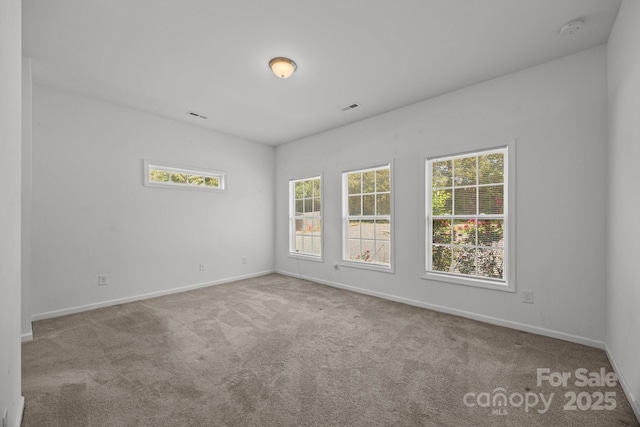 carpeted empty room with a healthy amount of sunlight, baseboards, and visible vents