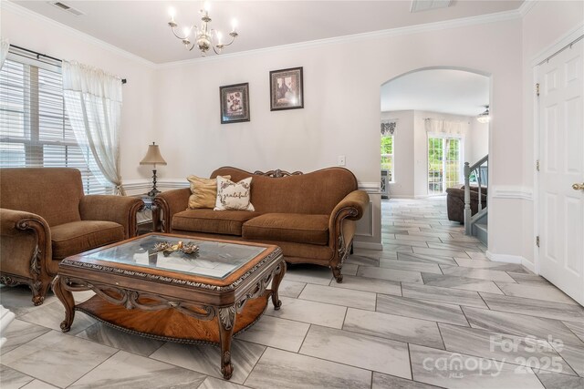 living area featuring an inviting chandelier, visible vents, baseboards, ornamental molding, and arched walkways
