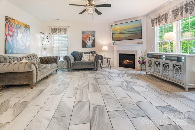 living area with a warm lit fireplace, a ceiling fan, and plenty of natural light