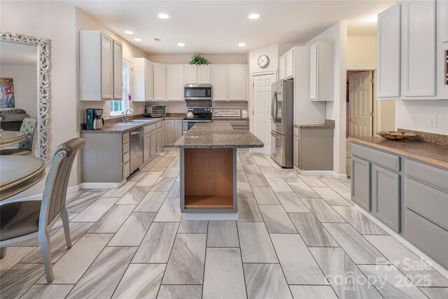 kitchen with dark stone countertops, recessed lighting, stainless steel appliances, a sink, and a center island