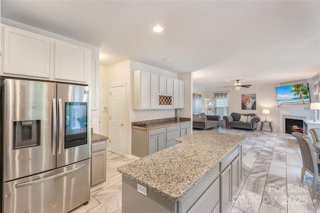 kitchen with light stone countertops, stainless steel fridge with ice dispenser, ceiling fan, a center island, and open floor plan