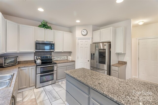 kitchen with light stone counters, a sink, appliances with stainless steel finishes, a toaster, and recessed lighting