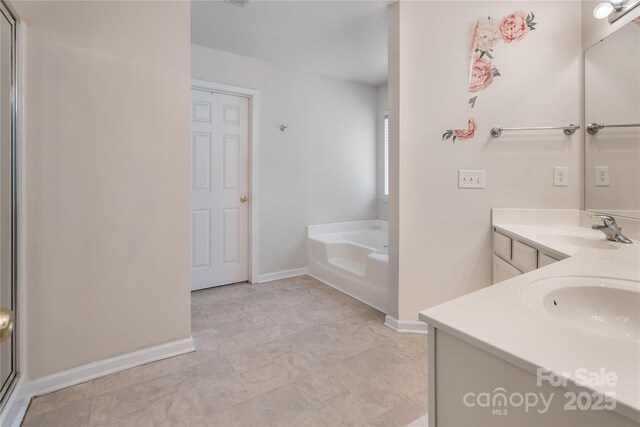 full bath with a garden tub, double vanity, a sink, and baseboards