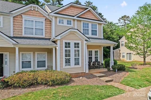 view of front facade with a front lawn, a shingled roof, and a patio