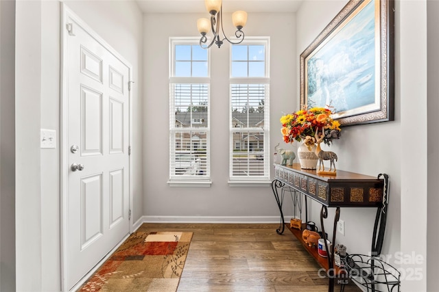 entryway with baseboards, wood finished floors, and an inviting chandelier