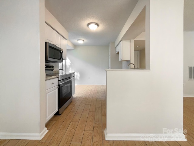kitchen featuring light wood finished floors, appliances with stainless steel finishes, baseboards, and white cabinetry