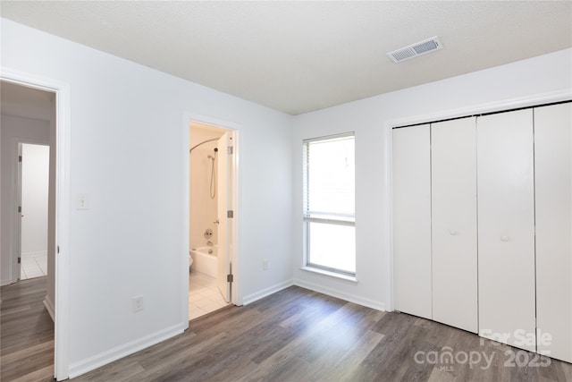 unfurnished bedroom with wood finished floors, a closet, connected bathroom, baseboards, and visible vents