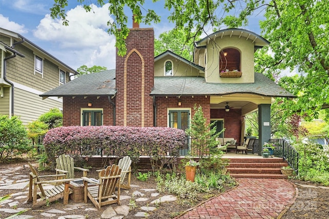 rear view of property featuring a chimney, ceiling fan, brick siding, an outdoor fire pit, and roof with shingles