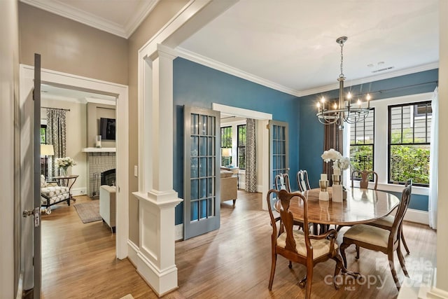 dining room featuring decorative columns, wood finished floors, a brick fireplace, and an inviting chandelier