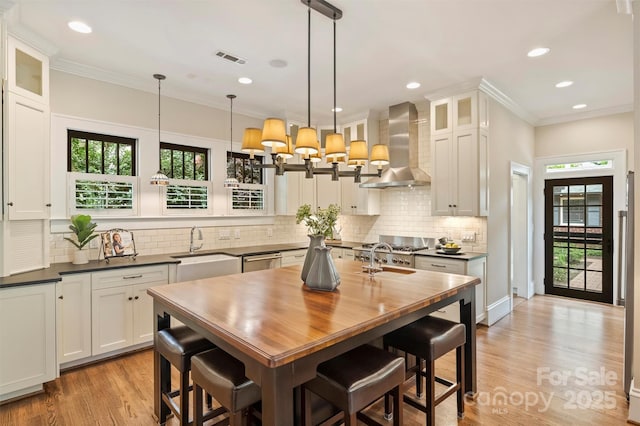 kitchen with wall chimney range hood, tasteful backsplash, a sink, dishwasher, and visible vents