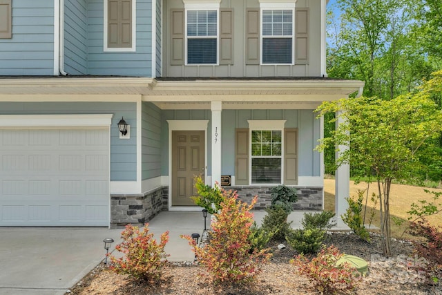 view of exterior entry featuring a porch, stone siding, concrete driveway, a garage, and board and batten siding