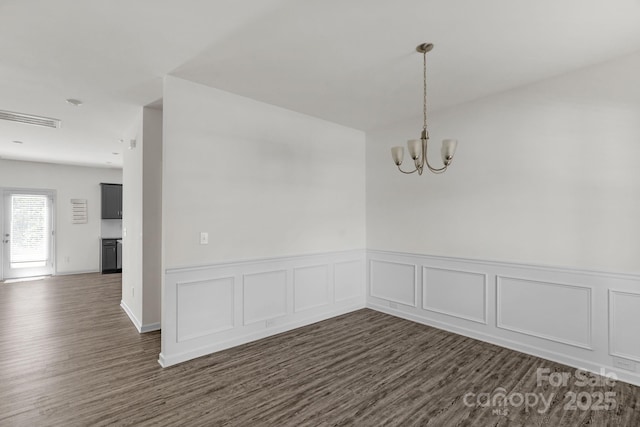 empty room featuring an inviting chandelier, visible vents, a wainscoted wall, and dark wood-style floors