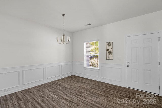 unfurnished dining area featuring a notable chandelier, a wainscoted wall, dark wood-type flooring, and visible vents