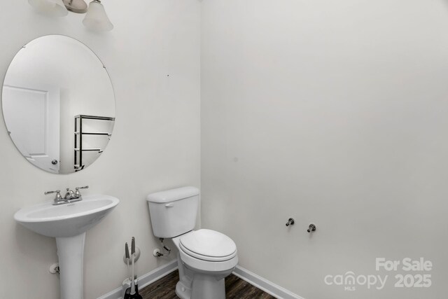 half bathroom featuring baseboards, wood finished floors, a sink, and toilet