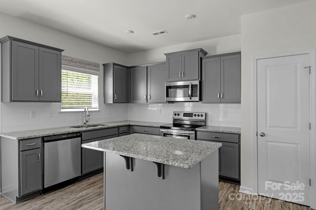 kitchen with light stone counters, gray cabinetry, stainless steel appliances, and a sink