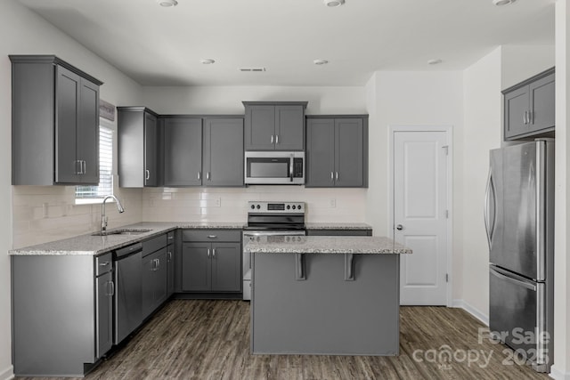 kitchen featuring stainless steel appliances, a sink, light stone counters, a kitchen island, and dark wood-type flooring