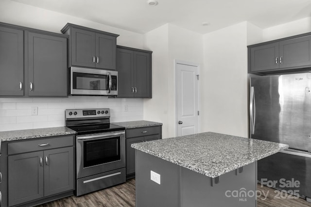 kitchen featuring dark wood finished floors, tasteful backsplash, appliances with stainless steel finishes, and light stone counters