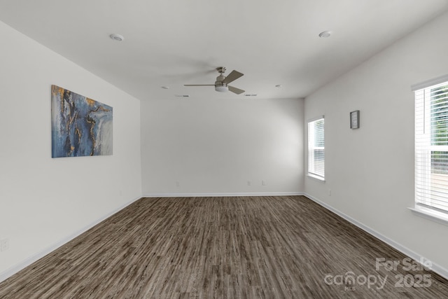 unfurnished room with dark wood finished floors, a wealth of natural light, a ceiling fan, and baseboards
