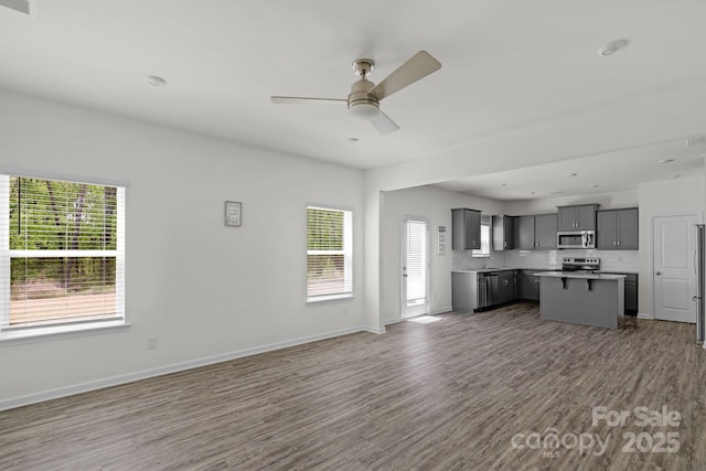 unfurnished living room featuring plenty of natural light, baseboards, wood finished floors, and ceiling fan