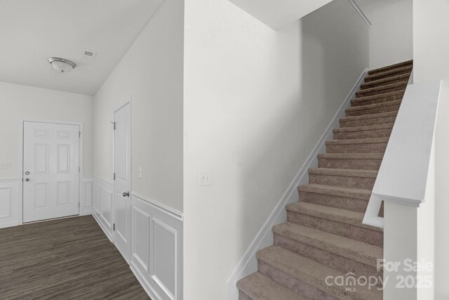 stairs featuring a decorative wall, wood finished floors, visible vents, and wainscoting
