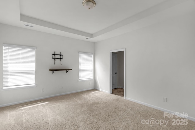 carpeted spare room with baseboards, visible vents, and a raised ceiling