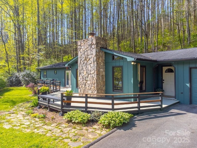 exterior space featuring board and batten siding, a chimney, a deck, and a wooded view