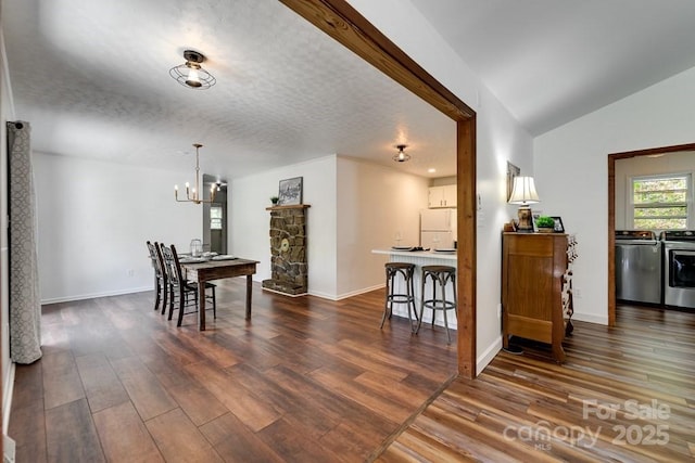 dining area with dark wood-style flooring, baseboards, a chandelier, washing machine and clothes dryer, and vaulted ceiling