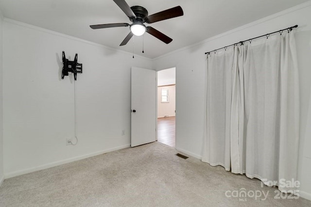 unfurnished room with carpet flooring, ceiling fan, baseboards, visible vents, and ornamental molding