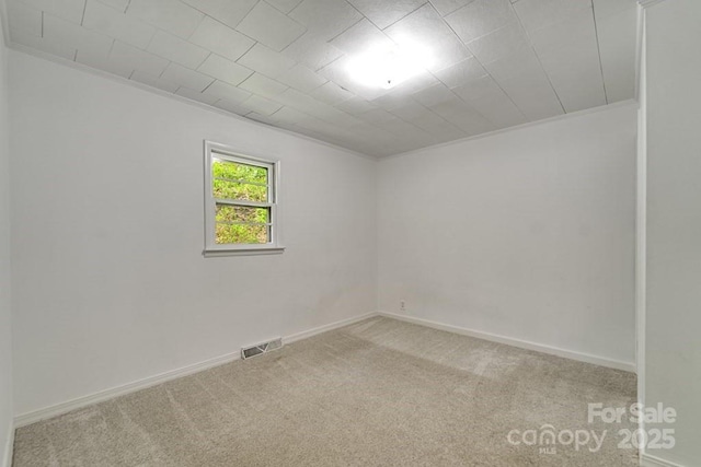 empty room featuring carpet flooring, baseboards, visible vents, and ornamental molding