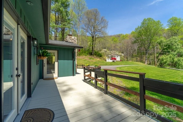 wooden terrace featuring a lawn and a view of trees