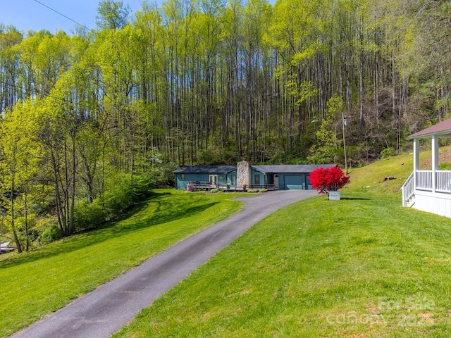 view of front facade with a view of trees, driveway, and a front yard