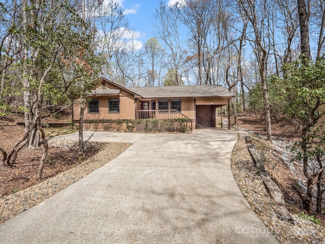 ranch-style home featuring concrete driveway, covered porch, roof with shingles, and a carport