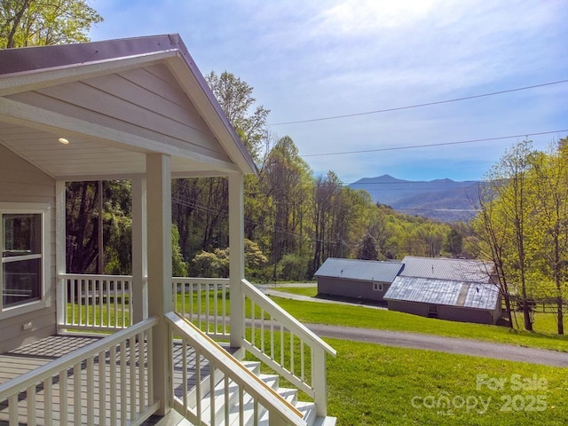 wooden deck with a mountain view, a yard, and a porch