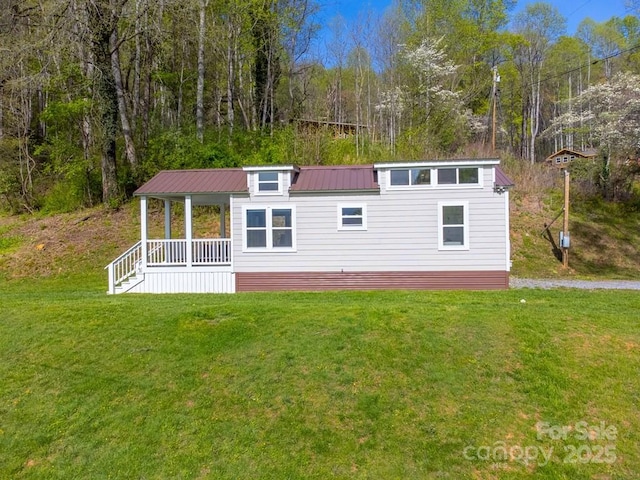 view of front facade featuring covered porch, a wooded view, metal roof, and a front yard