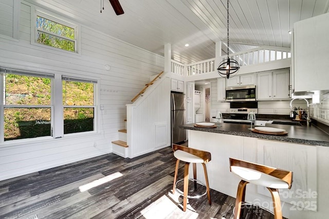 kitchen with dark countertops, vaulted ceiling, a sink, a peninsula, and stainless steel appliances