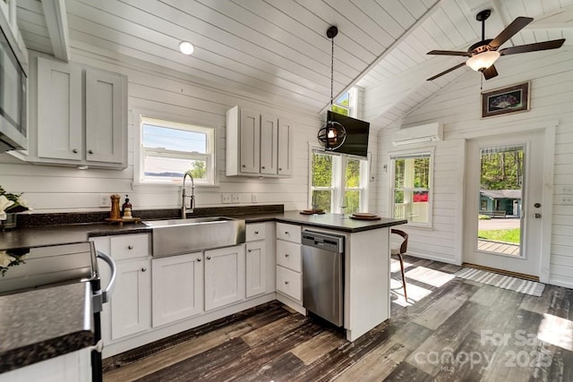 kitchen with dark countertops, a sink, a wall mounted air conditioner, a healthy amount of sunlight, and stainless steel dishwasher