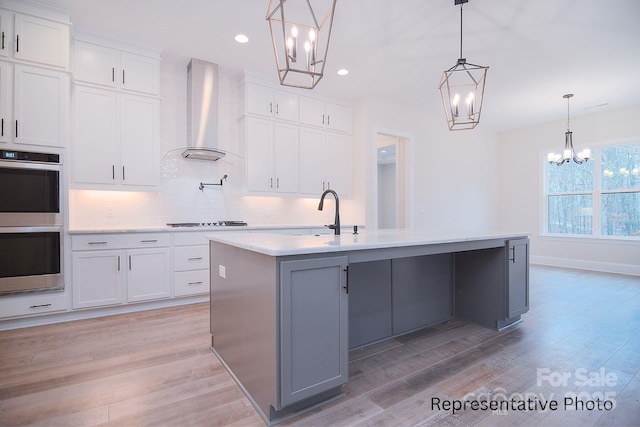 kitchen featuring wall chimney range hood, decorative backsplash, a sink, double oven, and a chandelier