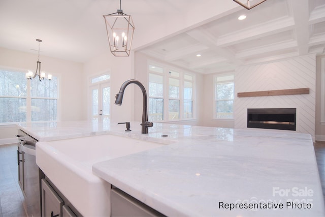 kitchen featuring a sink, light stone counters, beamed ceiling, and a notable chandelier