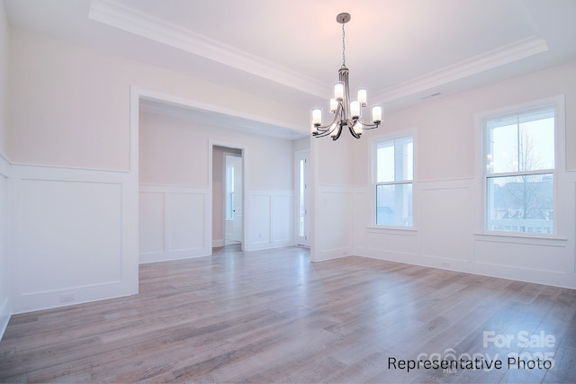 empty room featuring a tray ceiling, crown molding, wainscoting, an inviting chandelier, and a decorative wall