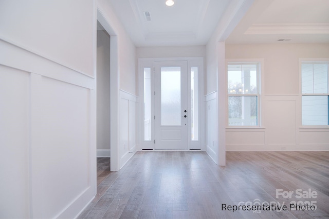 entryway with a tray ceiling, wood finished floors, and a decorative wall