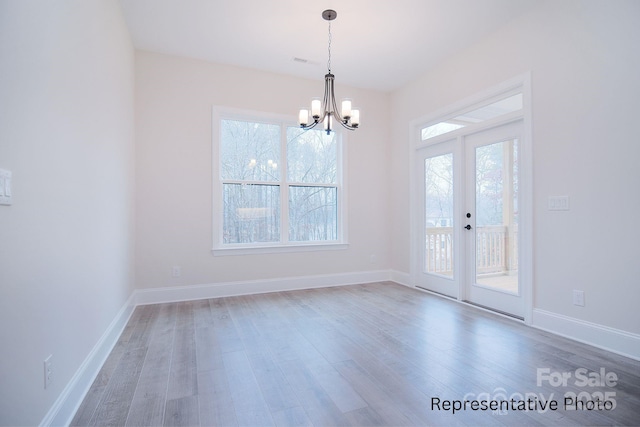unfurnished dining area with baseboards, wood finished floors, and a chandelier