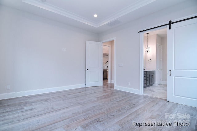 unfurnished bedroom featuring crown molding, a barn door, a raised ceiling, light wood-type flooring, and visible vents