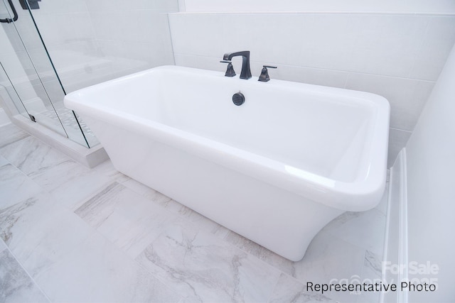 full bath with tile walls, a freestanding bath, a shower stall, and marble finish floor