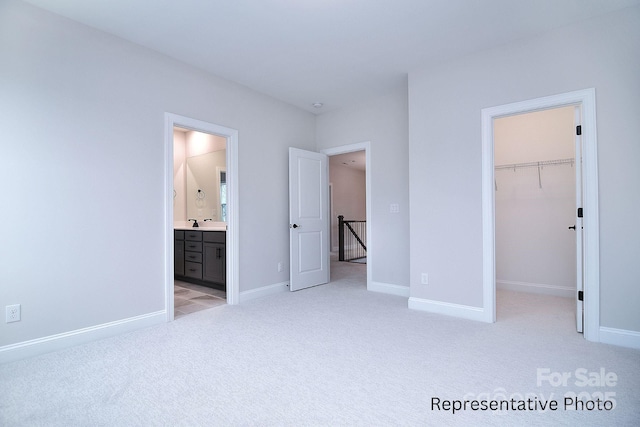 unfurnished bedroom with a closet, baseboards, a walk in closet, light colored carpet, and ensuite bath